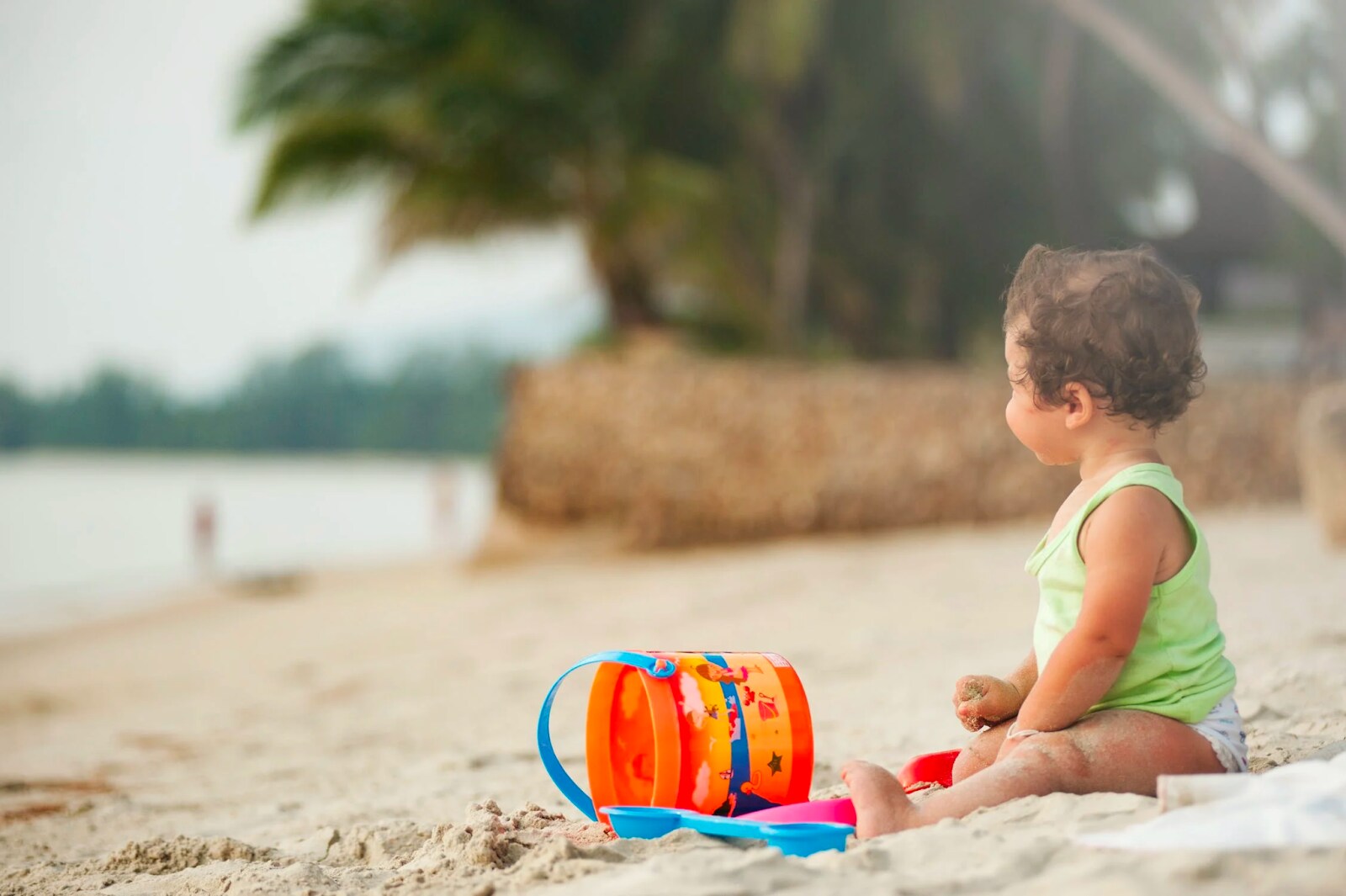 Little girl sitting on sand with toys